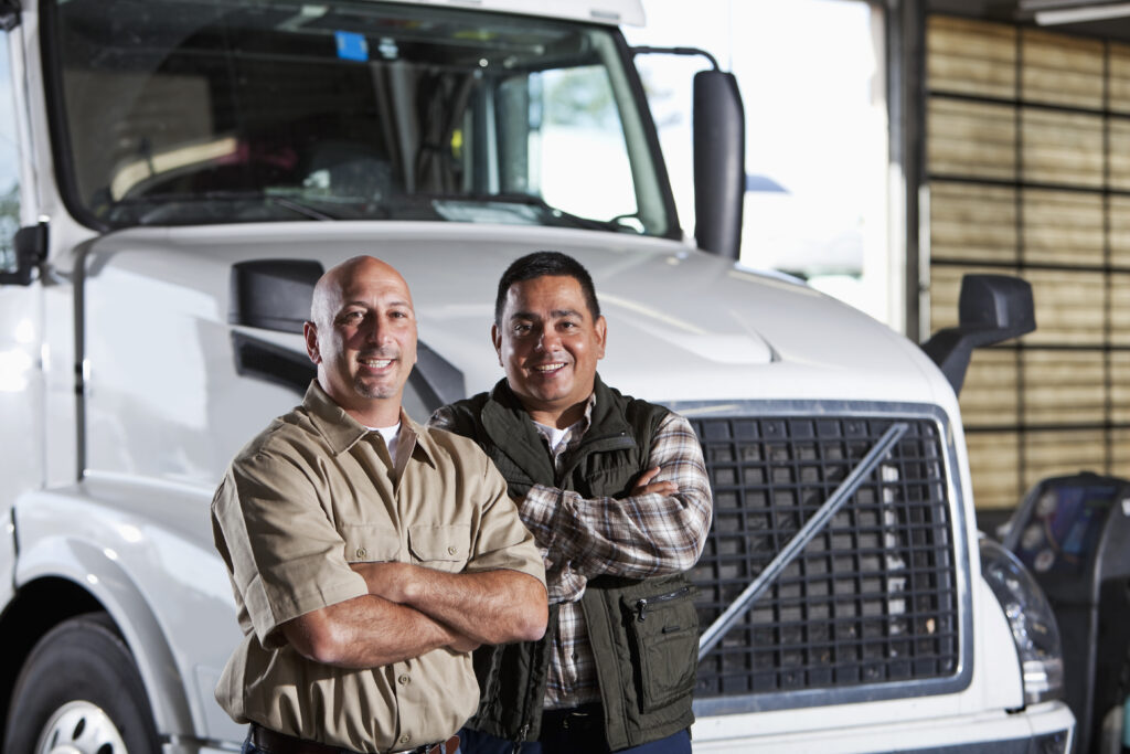 Two smiling truckers standing in front of a white semi truck